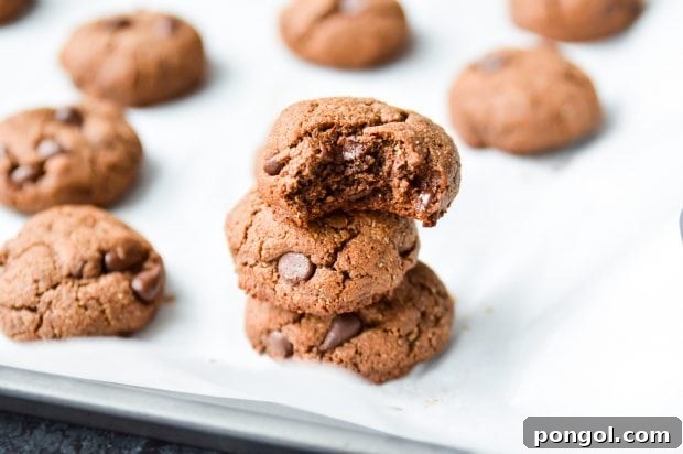 3 stacked Paleo Double Chocolate Fudge Cookies on a parchment paper-lined tray with more cookies in the background.