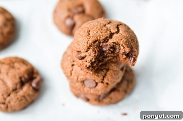 Close-up of three 3 stacked Paleo Double Chocolate Fudge Cookies on a parchment paper-lined tray with more cookies in the background.