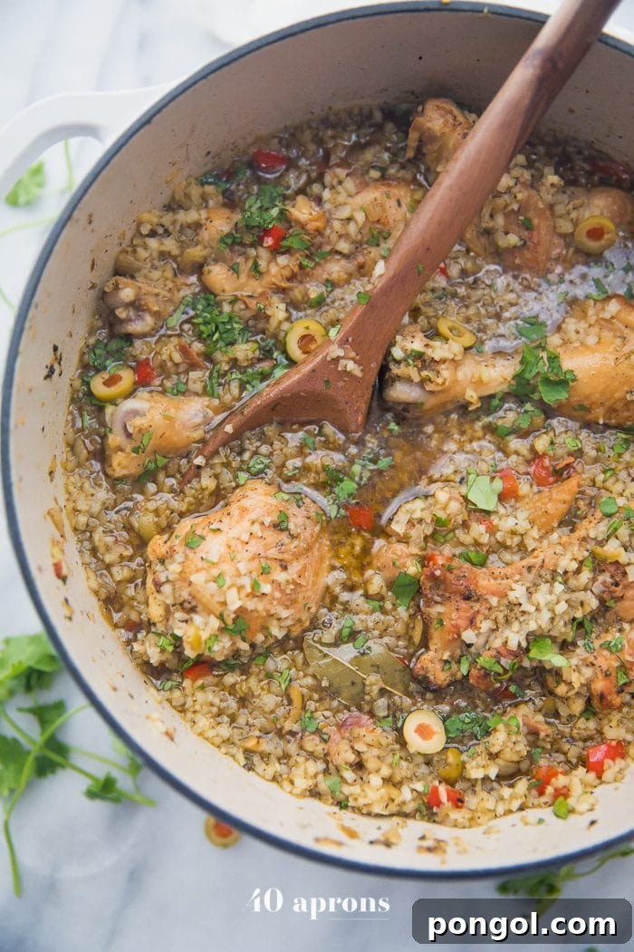 Close-up shot of a large pot brimming with healthy Spanish chicken and cauliflower rice stew, highlighting the tender chicken pieces, cauliflower rice, olives, and rich broth.