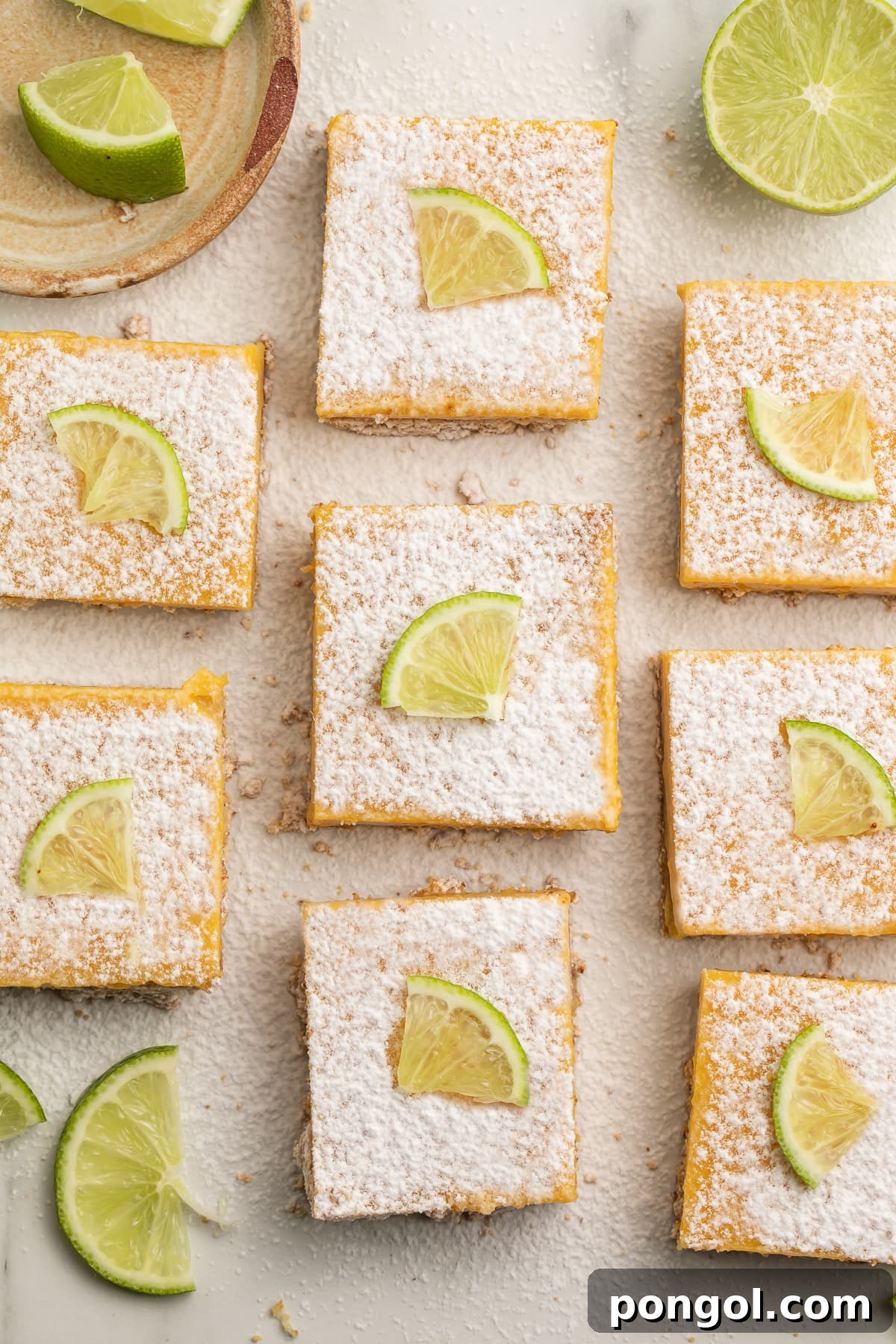 Tangy Paleo Lime Indulgence 3 Top down view of 8 paleo lime bars arranged neatly on a table, garnished with powdered sugar and fresh lime wedges, ready to be served.