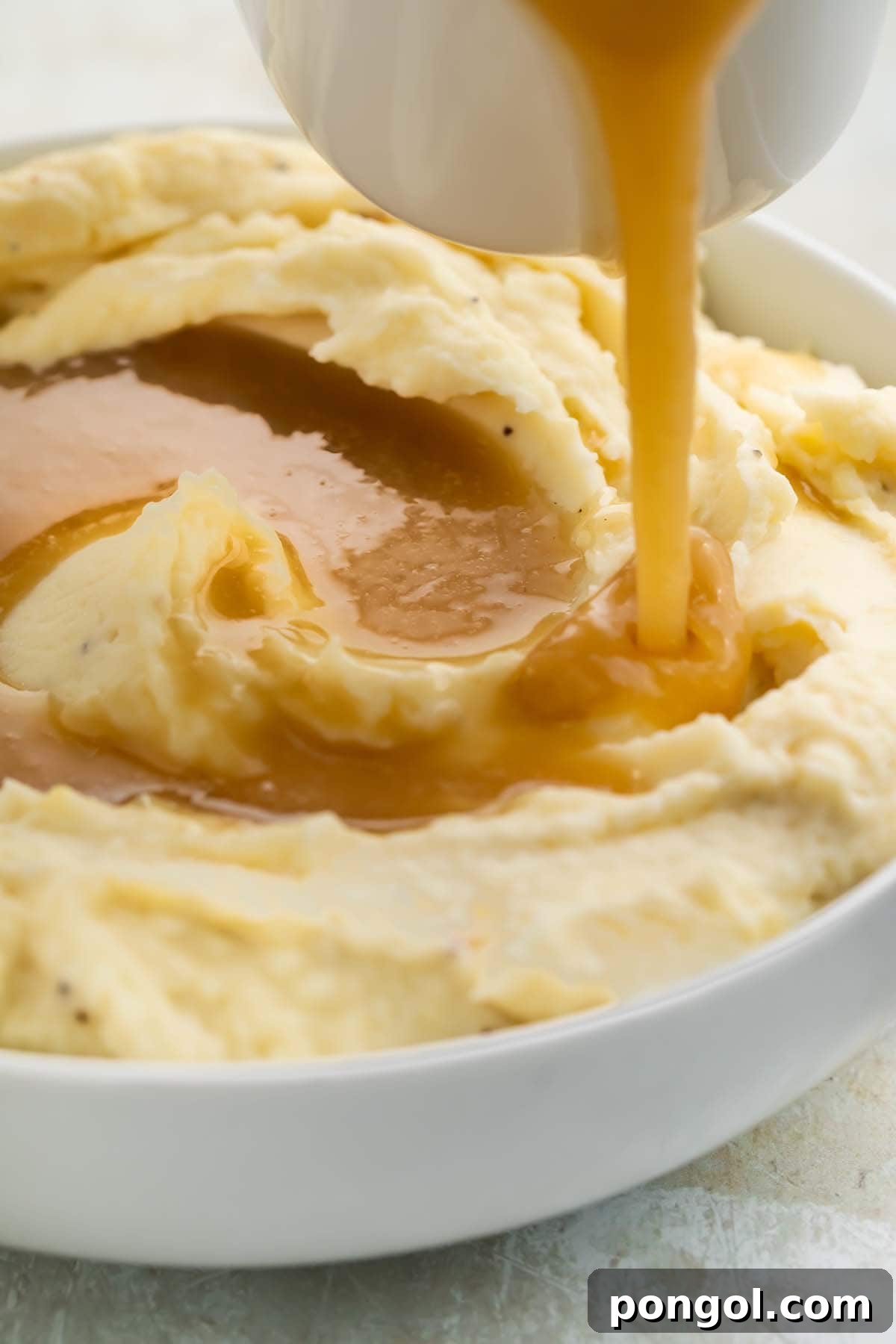 Paleo gravy being poured over a bowl of creamy mashed potatoes.