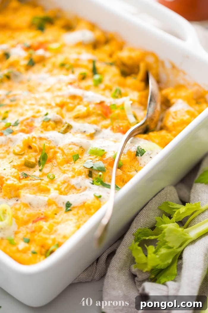 A close-up shot of the creamy Paleo Buffalo Chicken Casserole in a white baking dish, showing the rich texture and vibrant colors, with celery sticks subtly placed beside it.