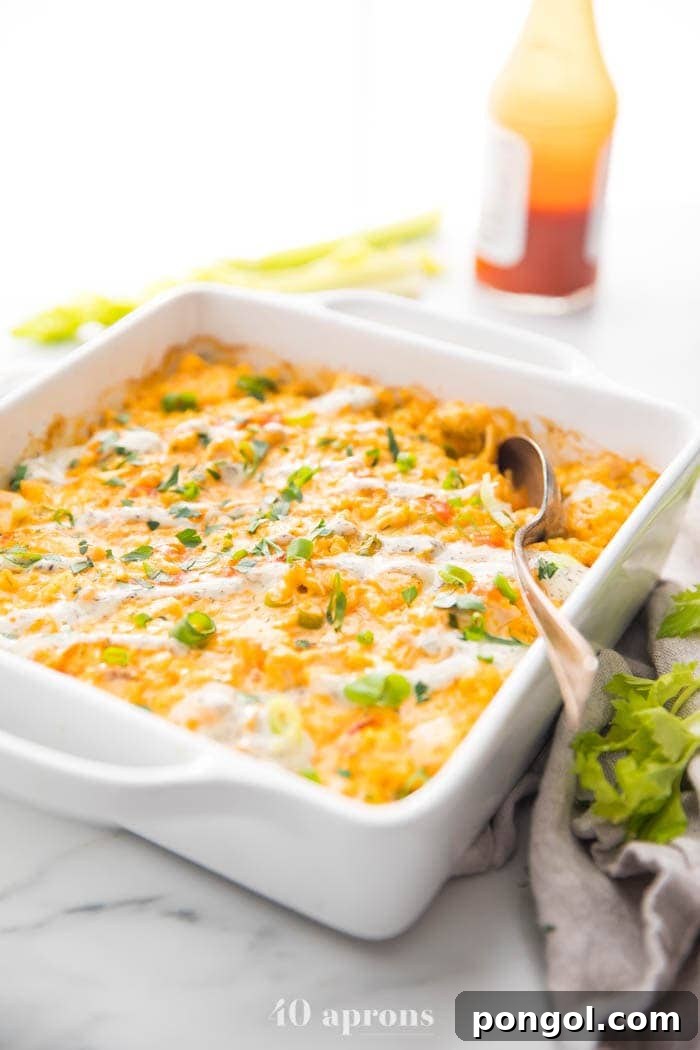 Close-up of a serving of Paleo Buffalo Chicken Casserole on a plate, with a bottle of hot sauce and fresh celery sticks in the background, highlighting the spicy and fresh components of the meal.