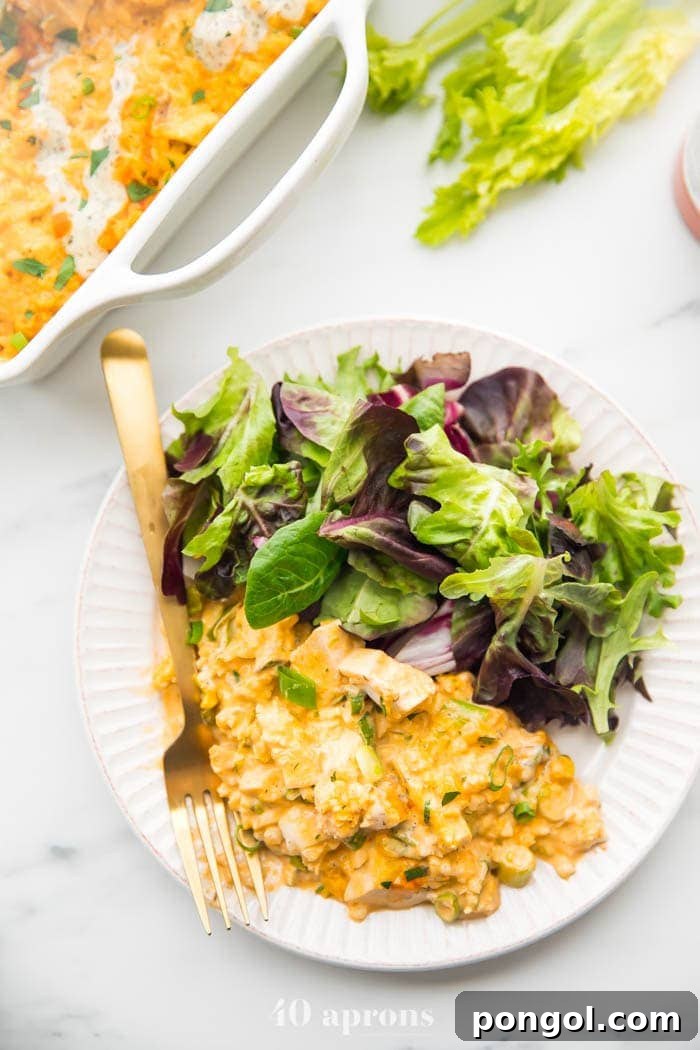 A freshly baked Paleo Buffalo Chicken Casserole on a plate with a side salad, presenting a complete and healthy meal, while the full casserole dish remains in the background.