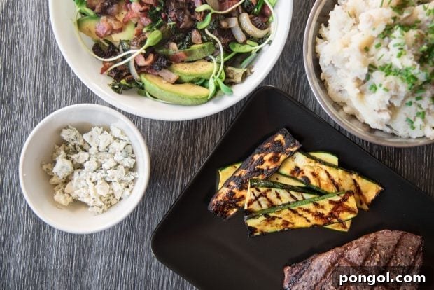 Sweet & Smoky Orange Glazed Zucchini (Paleo, Gluten Free) 3 Overhead shot of grill-marked orange glazed grilled zucchini slices arranged on a black plate next to a steak with more BBQ side dishes in the background.