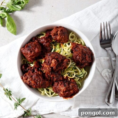 Whole30 Spaghetti and Meatballs served over zucchini noodles in a white bowl on a white tablecloth.