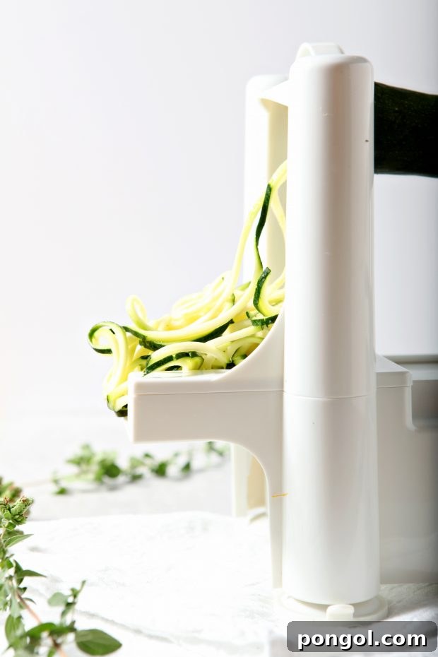 side view of zucchini being cut into zucchini noodles with a spiralizer