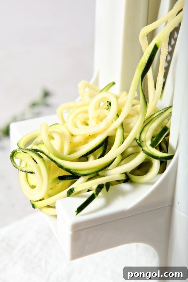 zucchini being cut into zucchini noodles with a spiralizer