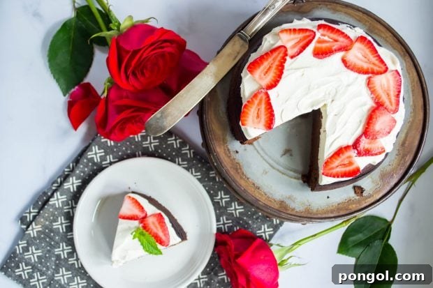overhead shot of a flourless paleo keto chocolate dessert torte on a cake stand with one slice cut, garnished with berries