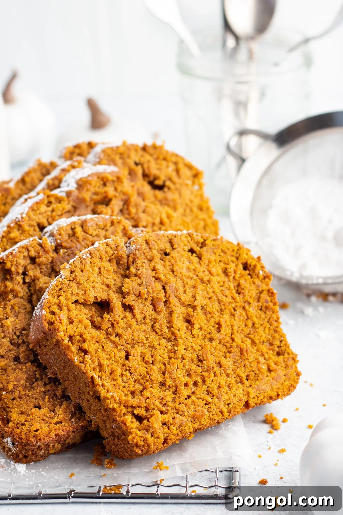 A side view of brightly colored orange slices of Gluten-Free Pumpkin Bread, delicately dusted with powdered sugar, artfully leaning against each other on a crisp white tabletop.