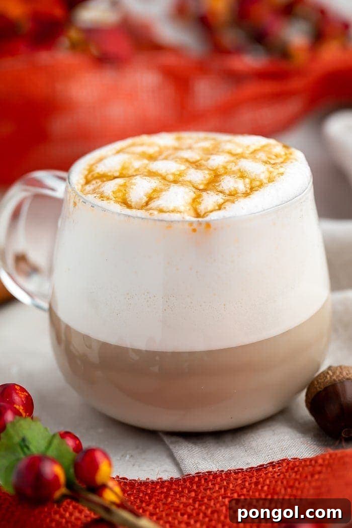 A pristine white coffee mug topped with a generous swirl of whipped cream and an artful caramel cross-stitch drizzle, suggesting a luxurious Plant-Based Pumpkin Caramel Macchiato.