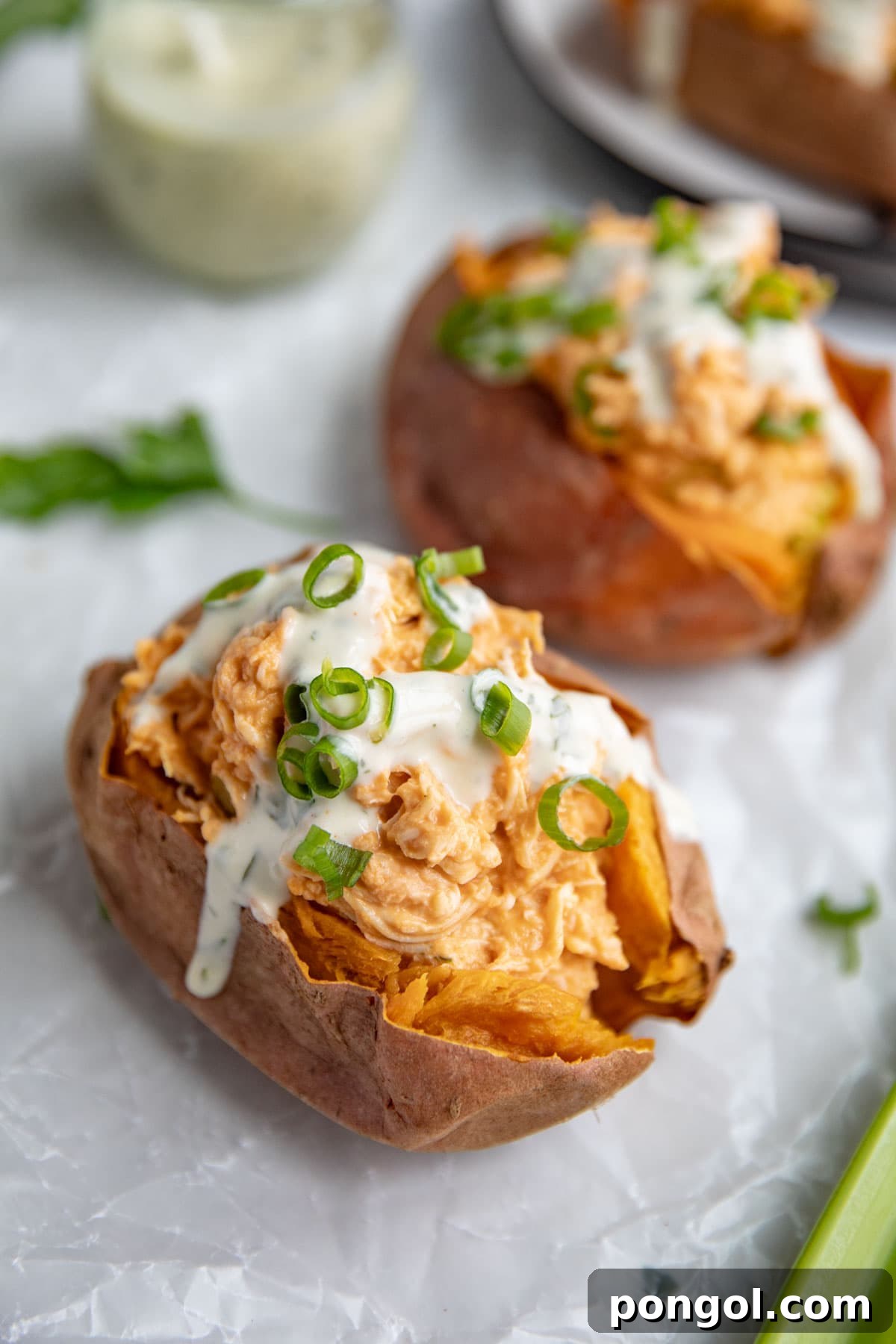 Buffalo chicken stuffed sweet potatoes topped with ranch dressing and green onions.