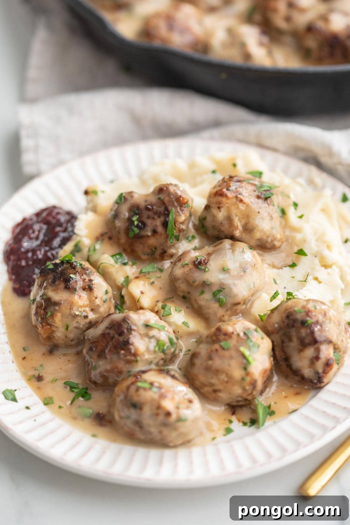 A plate of Whole30 Swedish meatballs and gravy atop a bed of mashed potatoes.
