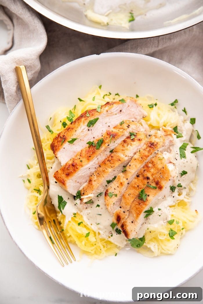 Healthy Whole30 chicken alfredo with spaghetti squash in a white bowl with a gold fork topped with parsley