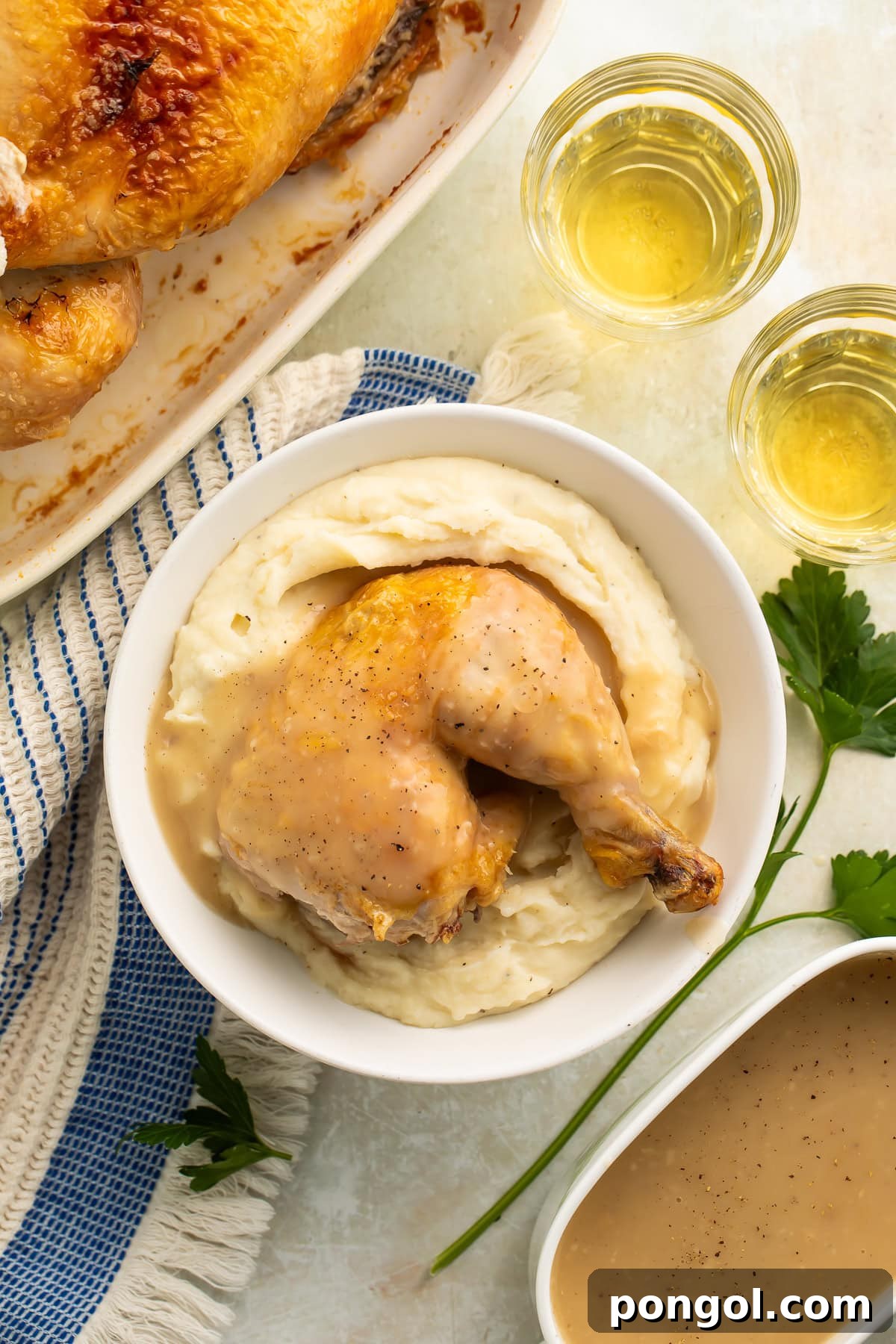 Golden roasted chicken leg and thigh with crispy skin on mashed potatoes in white bowl with gravy
