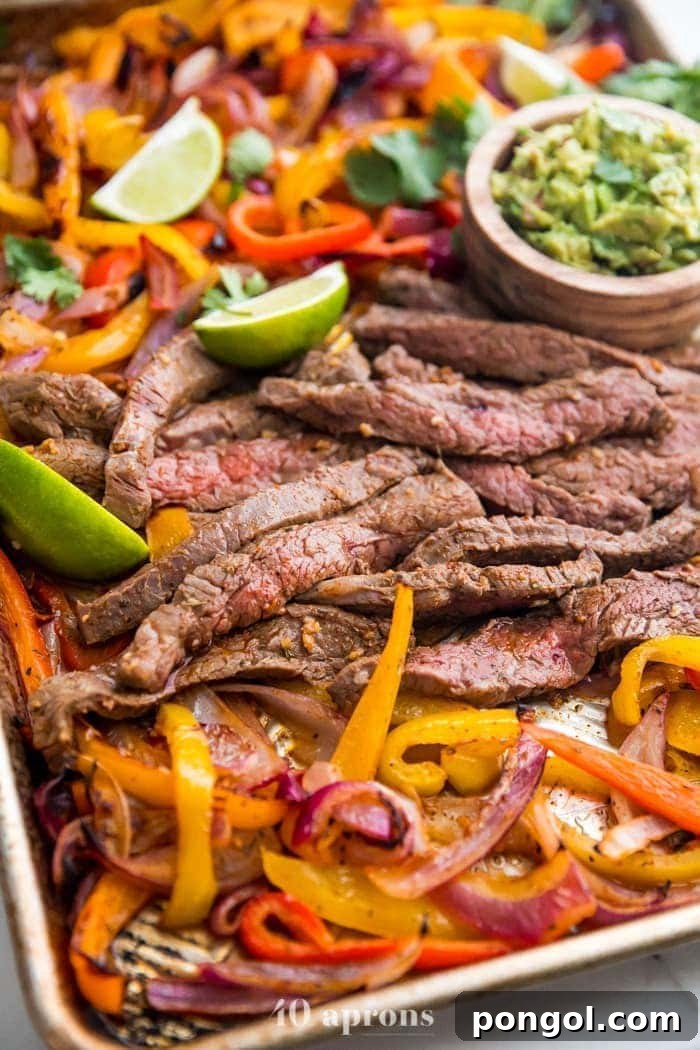 Best sheet pan fajitas with steak and peppers on a sheet pan with lime slices and guacamole off to the side