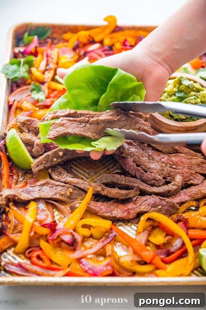 Best sheet pan fajitas with steak and peppers on a sheet pan with a hand putting steak in a lettuce cup