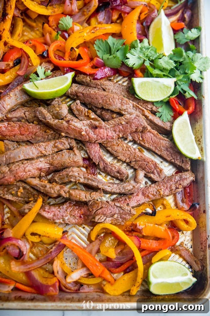 Best sheet pan fajitas with steak and peppers on a sheet pan with lime slices and guacamole off to the side