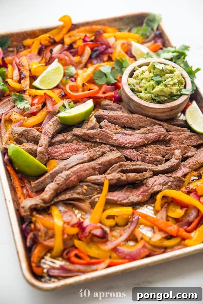 Best sheet pan fajitas with steak and peppers on a sheet pan with lime slices and guacamole off to the side