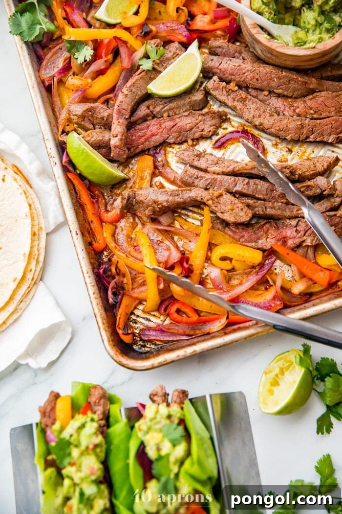 Best sheet pan fajitas with steak and peppers on a sheet pan with lime slices and guacamole off to the side