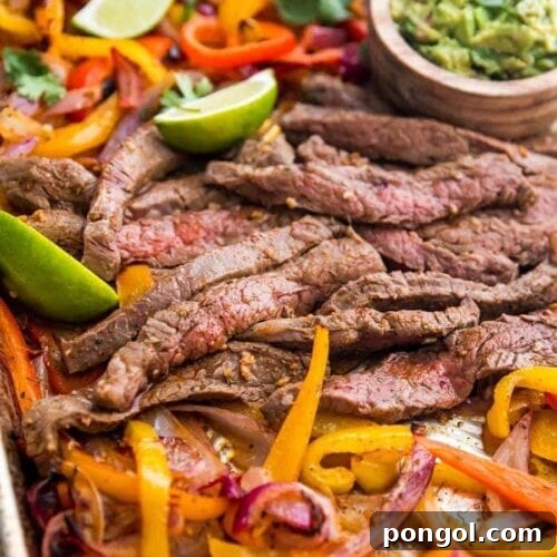 Best sheet pan fajitas with steak and peppers on a sheet pan with lime slices and guacamole off to the side
