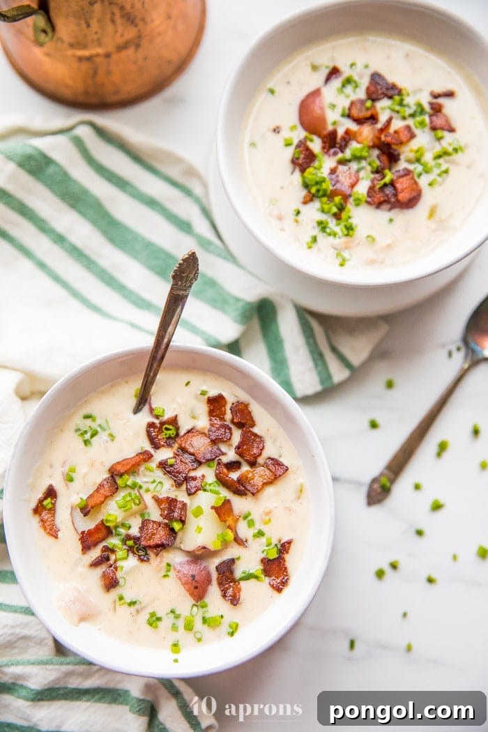 Overhead shot of healthy creamy Whole30 clam chowder in two bowls with crispy bacon and fresh chives, highlighting its rich texture and inviting presentation.