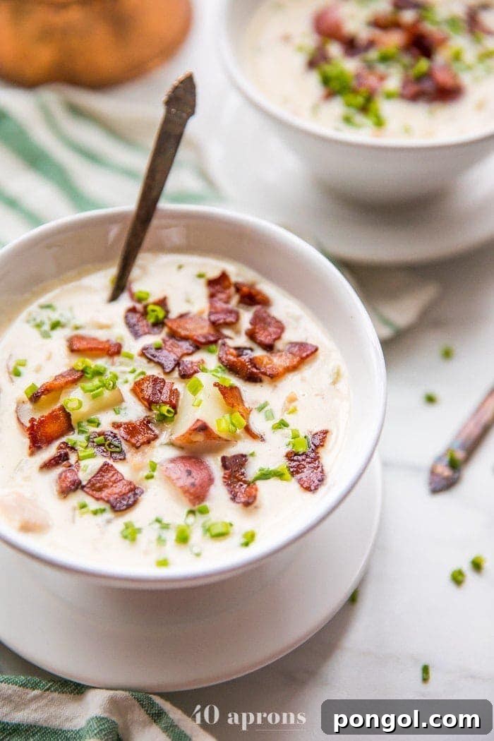 Close-up shot of a steaming bowl of healthy creamy Whole30 clam chowder, garnished with fresh chives and crispy bacon bits, showcasing its inviting texture.