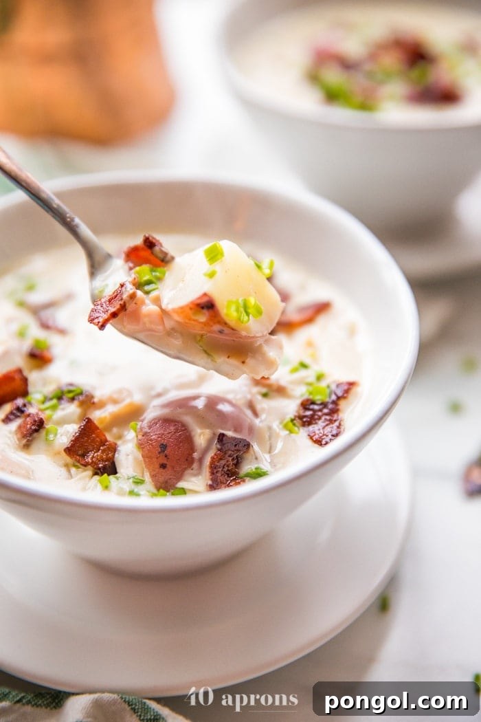 Close-up of a spoonful of creamy Whole30 clam chowder being lifted from a bowl, showing pieces of clam, potato, and bacon, with a focus on its appetizing consistency.