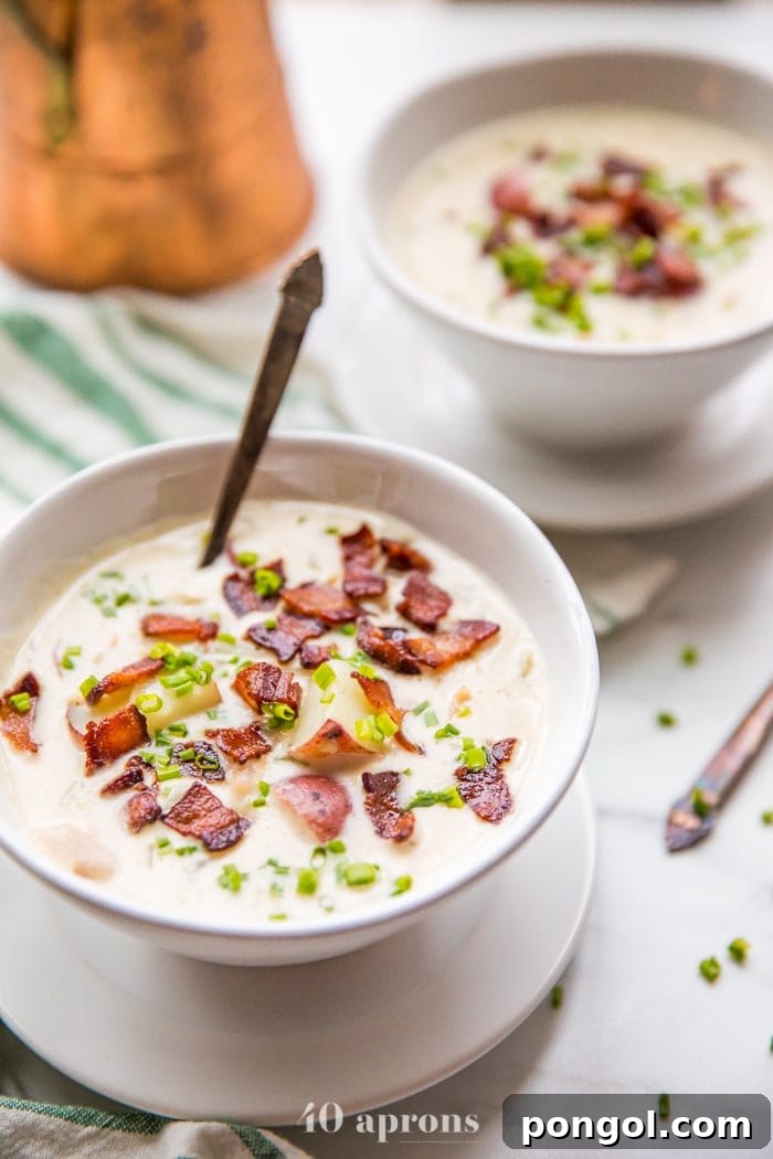 Two bowls of healthy creamy Whole30 clam chowder, perfectly garnished with crispy bacon and fresh chives, ready to be served on a rustic wooden surface.