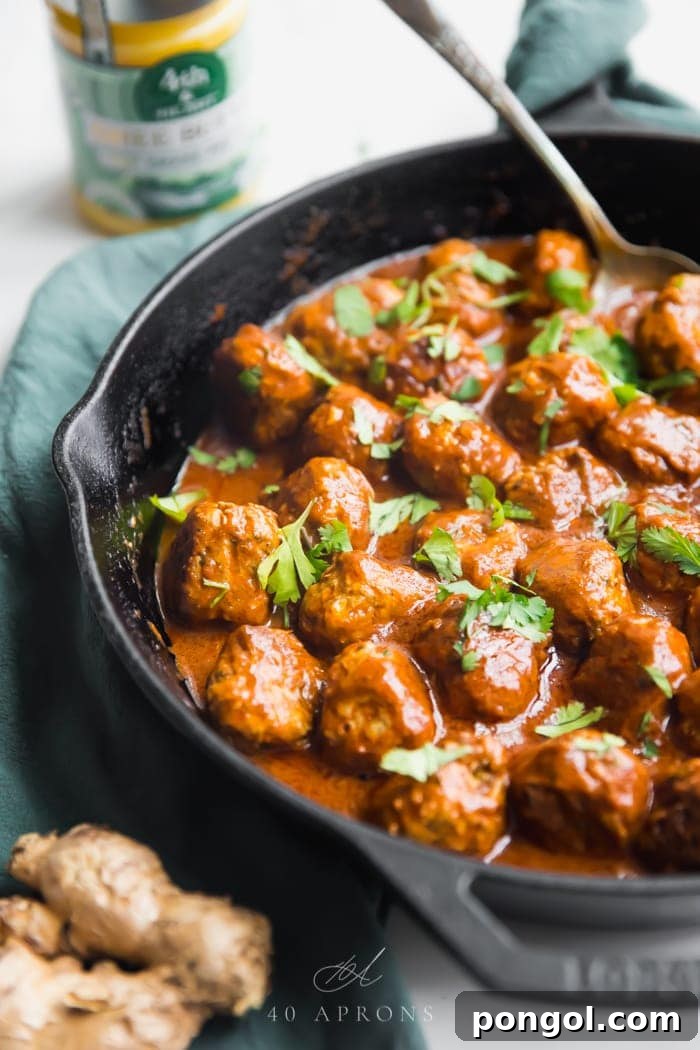 Indian meatballs with creamy sauce next to cauliflower rice topped with cilantro in a cast iron skillet on a green napkin