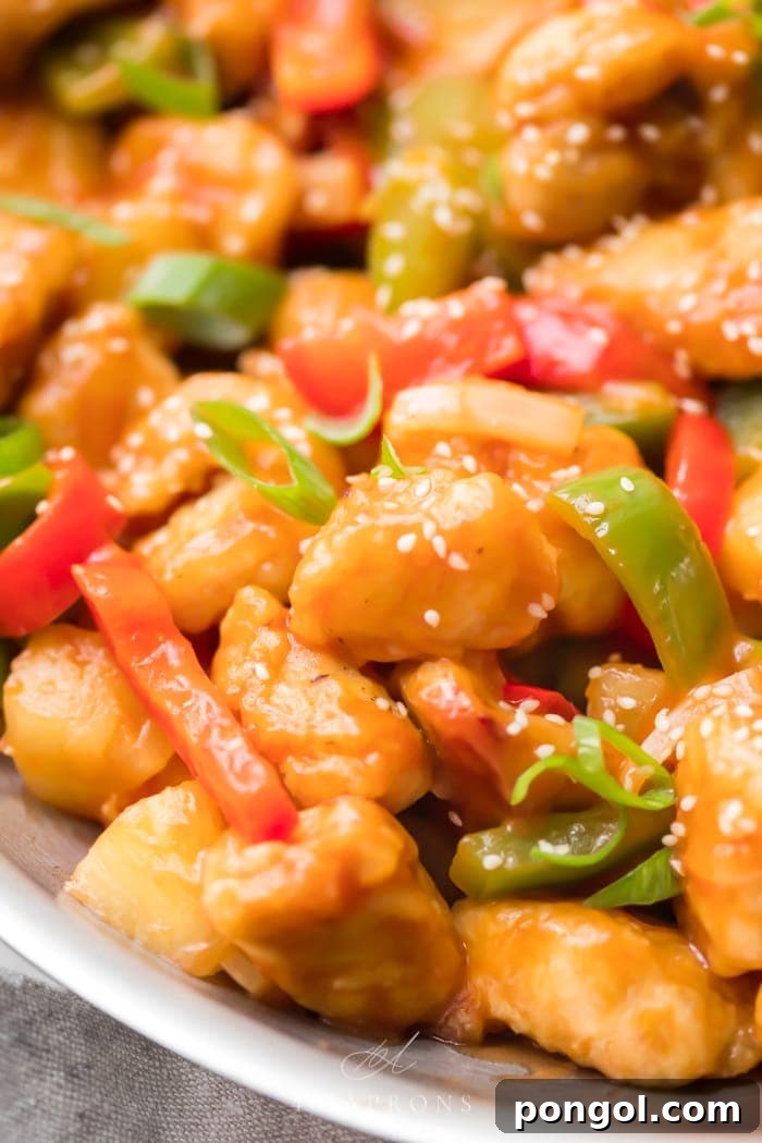A skillet of healthy sweet and sour chicken with vibrant red and green bell peppers, glistening with sauce