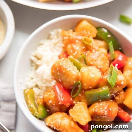 Healthy sweet and sour chicken with peppers over cauliflower rice in a white bowl with sesame seeds and chopsticks to the side