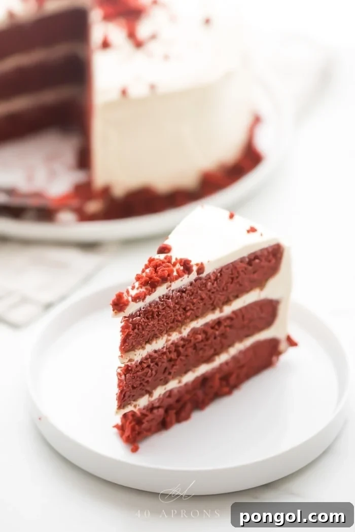 Slice of gluten free red velvet layer cake with paleo cream cheese frosting on a white plate with whole cake in background