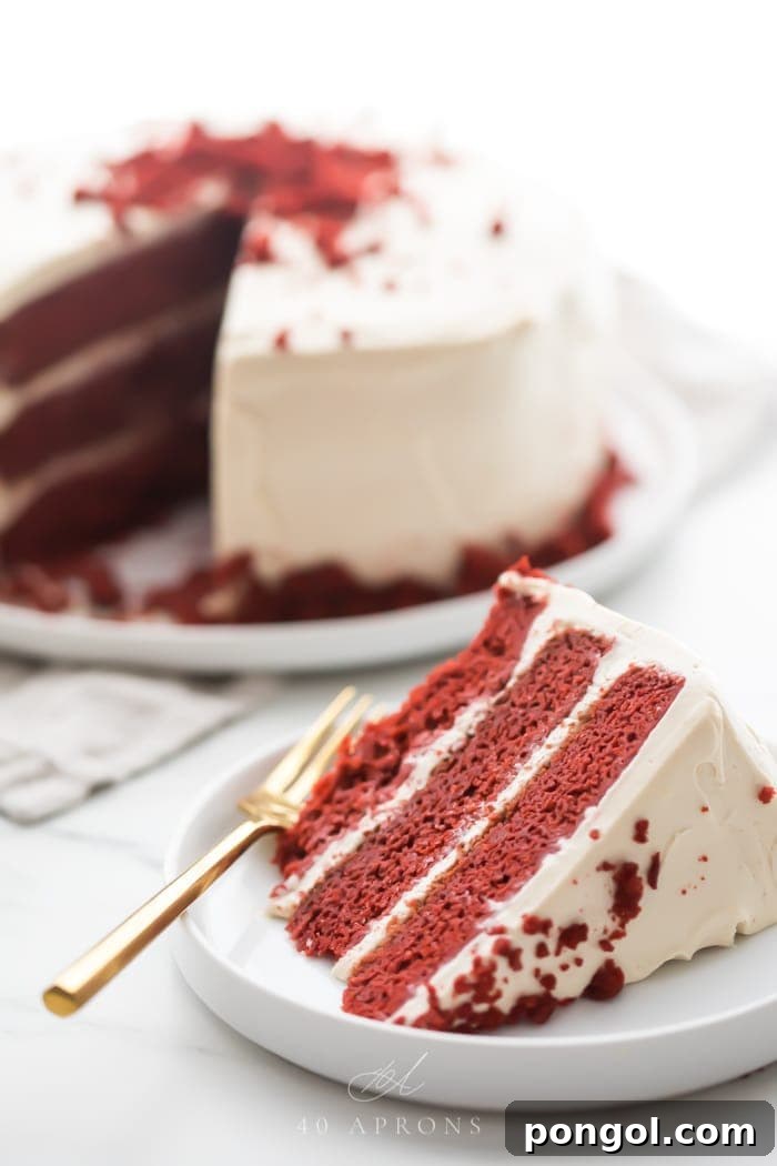 Slice of three layer gluten free red velvet cake with paleo cream cheese frosting on a white plate with whole cake in background