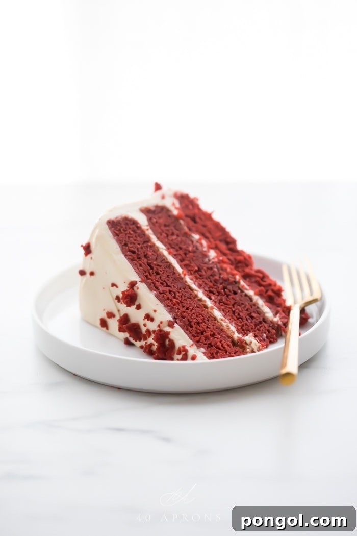 Slice of three layer gluten free red velvet cake with paleo cream cheese frosting on a white plate with a gold fork