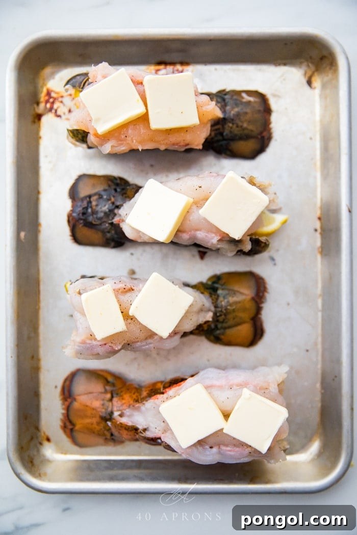Butterflied lobster tails on a baking sheet with pats of butter on top of each
