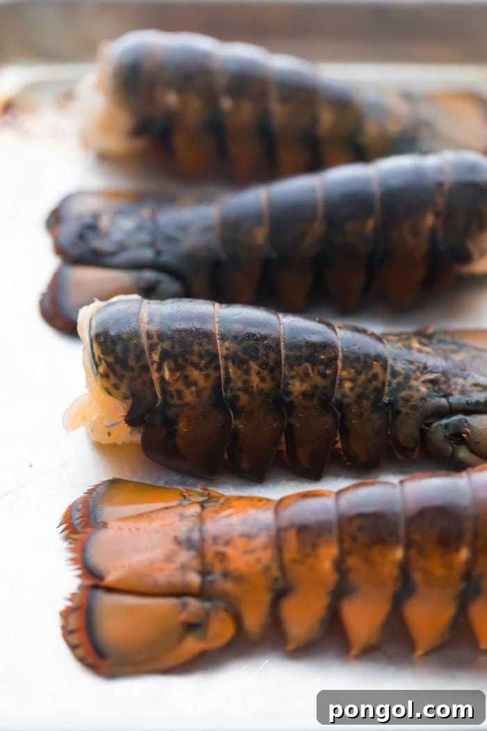 Four uncooked lobster tails on a baking sheet