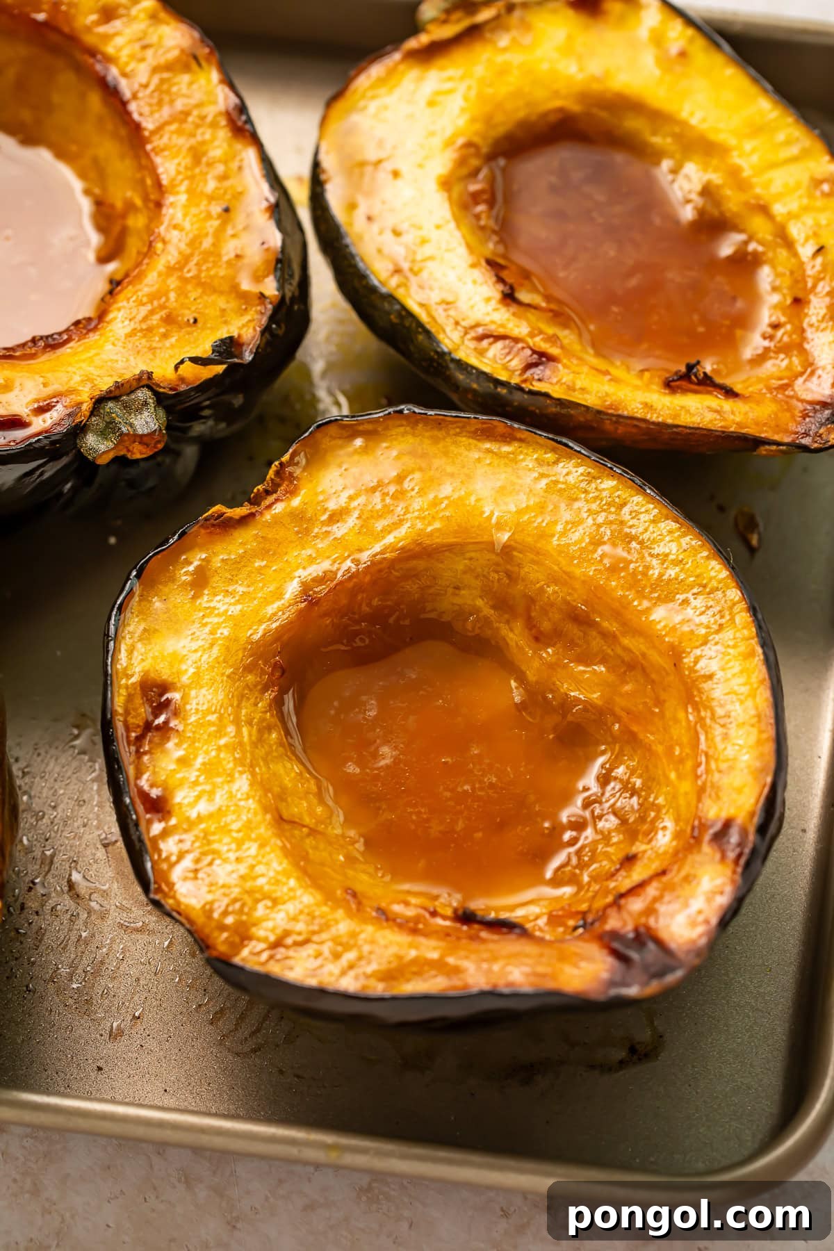 Roasted acorn squash halves with caramelized maple butter pooled in centers on baking sheet