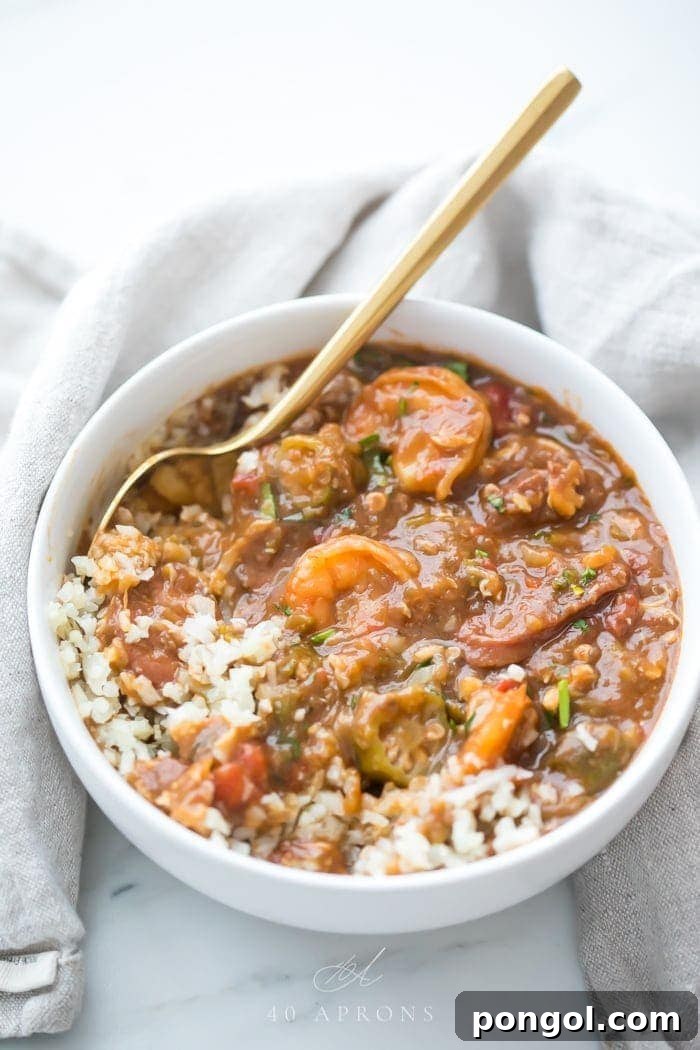 Healthy authentic seafood gumbo in a bowl with shrimp and okra over cauliflower rice in a white bowl with gold spoon