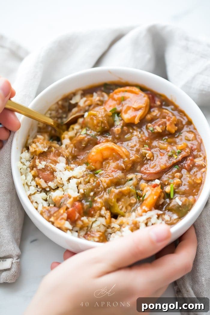 Hands holding a bowl of healthy authentic seafood gumbo with a white spoon over cauliflower rice