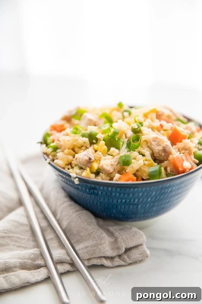 A small blue bowl of cauliflower fried rice with chicken, peas, carrots with a grey linen and silver chopsticks to the side