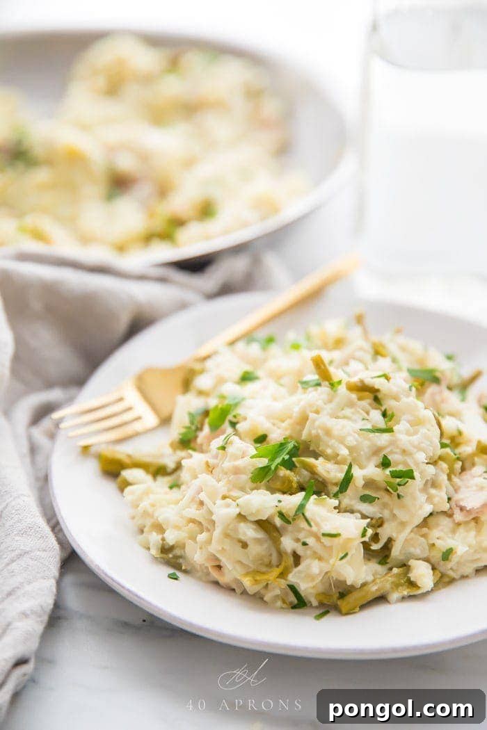 Quick creamy Whole30 cauliflower risotto with chicken and asparagus on a white plate with a gold fork, grey linen napkin next to the plate, and skillet with more risotto in the background