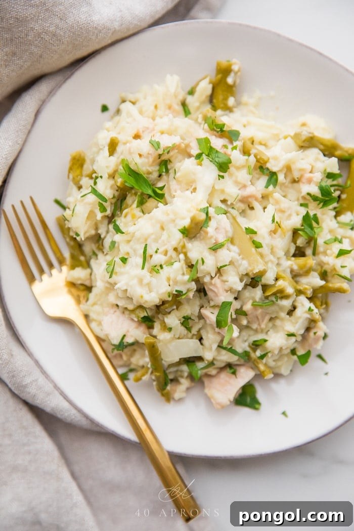 Quick creamy Whole30 cauliflower risotto with chicken and asparagus on a white plate with a gold fork, grey linen napkin next to the plate