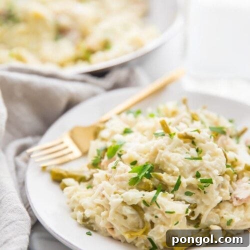 Quick creamy Whole30 cauliflower risotto with chicken and asparagus on a white plate with a gold fork, grey linen napkin next to the plate, and skillet with more risotto in the background