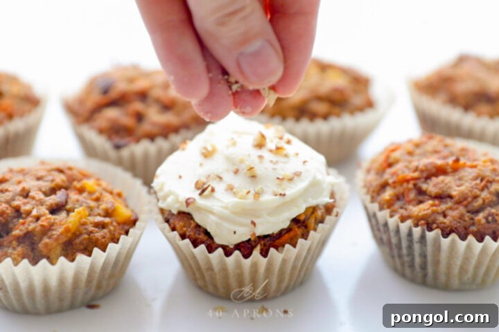 Delicious Paleo Carrot Cake Cupcakes Free From Gluten and Dairy 12 A white woman's hand sprinkling finely chopped pecans onto the top of frosted carrot cake cupcakes.