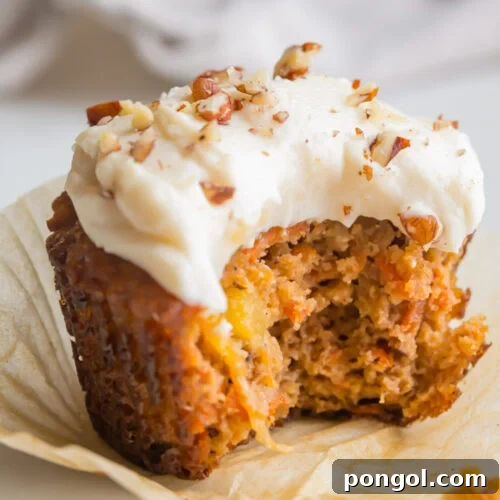 Delicious Paleo Carrot Cake Cupcakes Free From Gluten and Dairy 5 A paleo carrot cake cupcake topped with cream cheese frosting and chopped pecans. A bite is missing from the cupcake.