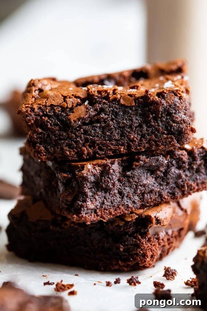 Ultimate Fudgy Crackly Paleo Brownies Gluten Free 2 A stack of three paleo brownies showing how fudgy and rich they are, with a crackly top and flake sea salt on top