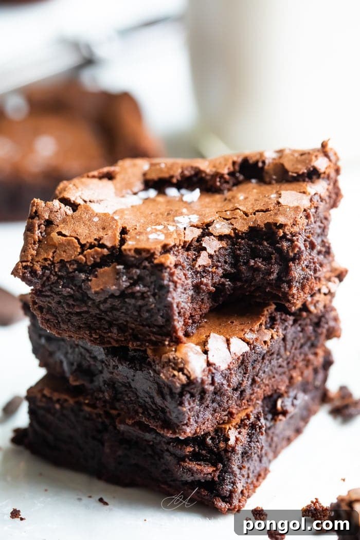 Ultimate Fudgy Crackly Paleo Brownies Gluten Free 6 A stack of three gluten free, paleo brownies showing how fudgy and rich they are, with a crackly top and flake sea salt on top and a bite out of one