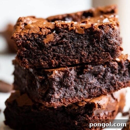 A stack of three paleo brownies showing how fudgy and rich they are, with a crackly top and flake sea salt on top