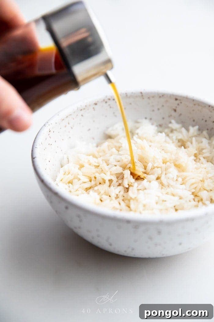 A bottle of soy sauce substitute pouring over a bowl of white rice, highlighting its rich, dark color and versatility as a condiment.